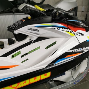 May include: A white, black, blue, orange and yellow jet ski with the words "RIVA RACING", "PIRANHA" and "12 Jet Pilot" on the side.
