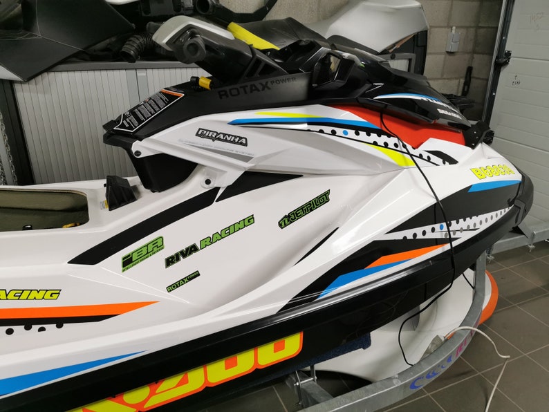 May include: A white, black, blue, orange and yellow jet ski with the words "RIVA RACING", "PIRANHA" and "12 Jet Pilot" on the side.