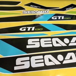 以下が含まれることがあります： 青と緑のアクセントが付いた白黒のシー-ドゥーデカール。デカールには「シー-ドゥー」、「GTI 130」、「ROTAX」の文字が書かれています。