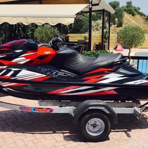 May include: A black and red jet ski with white accents and the text "RXP-X 260" on the side. The jet ski is on a trailer with the text "U.S. Trailer" on the side.