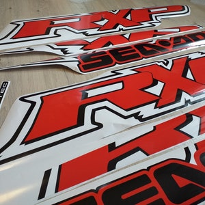 May include: A set of red and black vinyl decals with the words "RXP" and "Sea-Doo" printed on them. The decals are designed for use on a watercraft.