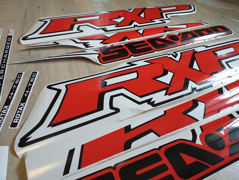 May include: A set of red and black vinyl decals with the words "RXP" and "Sea-Doo" printed on them. The decals are designed for use on a watercraft.