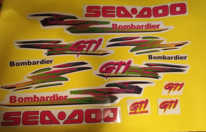 May include: A set of Sea-Doo GTI decals in various colors, including red, pink, green, black, and yellow. The decals feature the Sea-Doo logo, the GTI logo, and the Bombardier logo. The decals are designed for a Sea-Doo GTI personal watercraft.