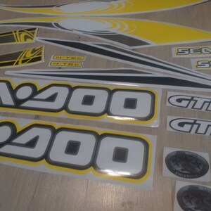 May include: A set of black, white, and yellow Sea-Doo GTI decals. The decals feature the text "Sea-Doo", "GTI", and "Sea-Doo GTI".