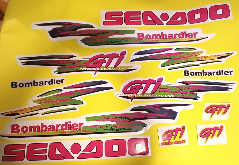 May include: A set of Sea-Doo GTI decals in pink, green, black, and white. The decals feature the Sea-Doo logo, the words "Sea-Doo", "GTI", "Bombardier", and "Powered by Rotax Marine".