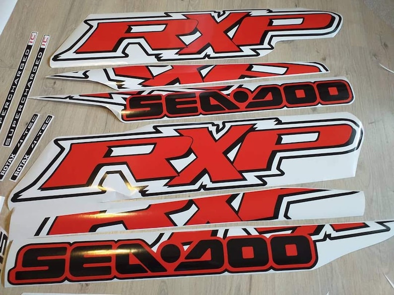 May include: A set of red and black vinyl decals for a Sea-Doo RXP watercraft. The decals feature the words "Sea-Doo" and "RXP" in a bold, stylized font. The decals are designed to be applied to the hull of the watercraft.
