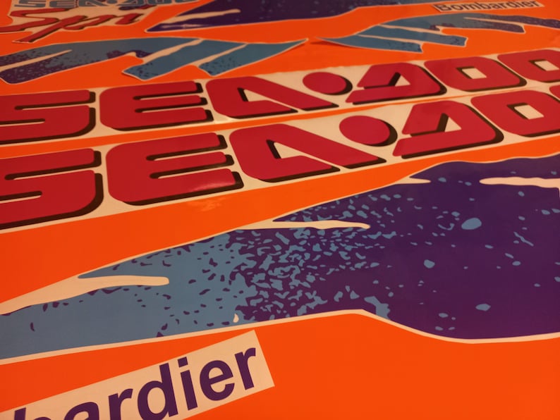 K&ouml;nnte beinhalten: Ein Satz pinkfarbener und schwarzer Sea-Doo-Aufkleber mit einem blauen und violetten Grafikdesign. Die Aufkleber befinden sich auf einem orangefarbenen Hintergrund.