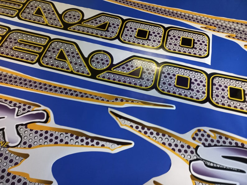 Puede incluir: Primer plano de una calcoman&iacute;a de motocicleta con un dise&ntilde;o negro y amarillo. La calcoman&iacute;a presenta un patr&oacute;n repetitivo de c&iacute;rculos y cuadrados con un fondo blanco. El texto "2000" es visible en el dise&ntilde;o.