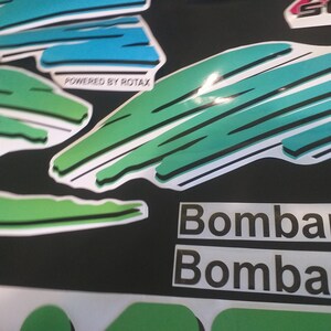 Puede incluir: Pegatinas gr&aacute;ficas verdes y azules con el texto "Powered by Rotax" y "Bombardier" repetido dos veces.