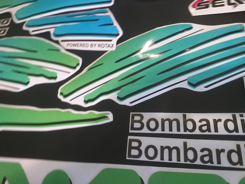 Puede incluir: Pegatinas gr&aacute;ficas verdes y azules con el texto "Powered by Rotax" y "Bombardier" repetido dos veces.