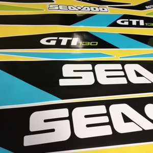 以下が含まれることがあります： 青と緑のアクセントが付いた白黒のシー-ドゥーデカール。デカールには、シー-ドゥーのロゴと「シー-ドゥー」、「GTI 130」、「ROTAX」の文字が書かれています。