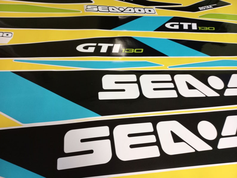 以下が含まれることがあります： 青と緑のアクセントが付いた白黒のシー-ドゥーデカール。デカールには、シー-ドゥーのロゴと「シー-ドゥー」、「GTI 130」、「ROTAX」の文字が書かれています。