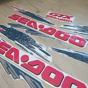 K&ouml;nnte beinhalten: Ein Satz roter und wei&szlig;er Sea-Doo-Aufkleber mit einem grau-wei&szlig;en grafischen Design. Die Aufkleber enthalten den Text "Sea-Doo" und "GTX Sea-Doo".
