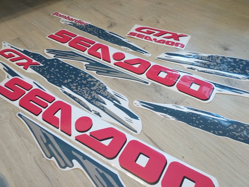 K&ouml;nnte beinhalten: Ein Satz roter und wei&szlig;er Sea-Doo-Aufkleber mit einem grau-wei&szlig;en grafischen Design. Die Aufkleber enthalten den Text "Sea-Doo" und "GTX Sea-Doo".