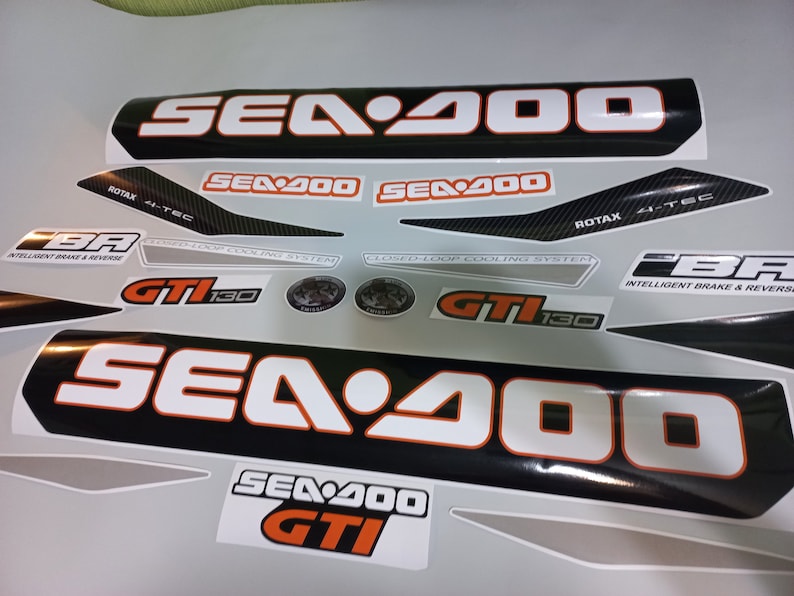 May include: A set of black and white Sea-Doo decals with orange accents. The decals feature the Sea-Doo logo, the text "Sea-Doo", "Sea-Doo GTI", "GTI 130", "Intelligent Brake & Reverse", and "Closed-Loop Cooling System".