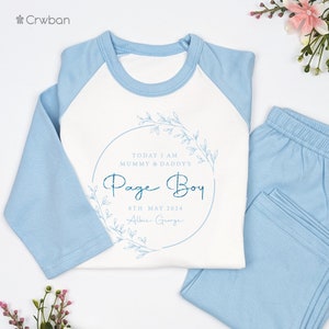 May include: A light blue and white pajama set. The top has light blue sleeves and a white body with the text "Today I am Mummy & Daddy's Page Boy" inside a floral wreath. The matching pants are light blue.