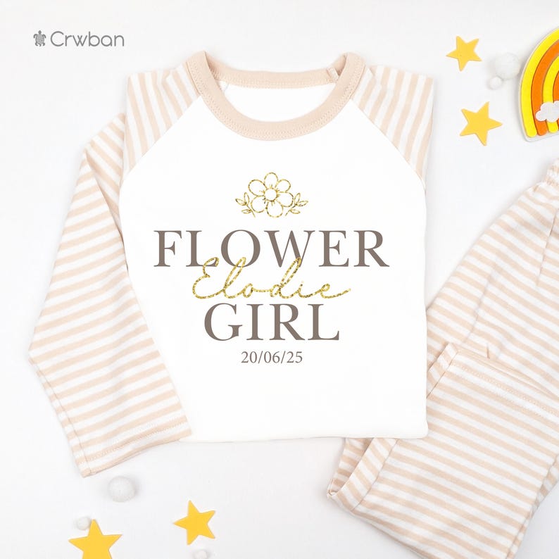 May include: A white long-sleeved top and matching trousers set with a beige and white striped pattern. The top features the text "FLOWER Elodie GIRL" with a flower graphic and the date 20/06/25.
