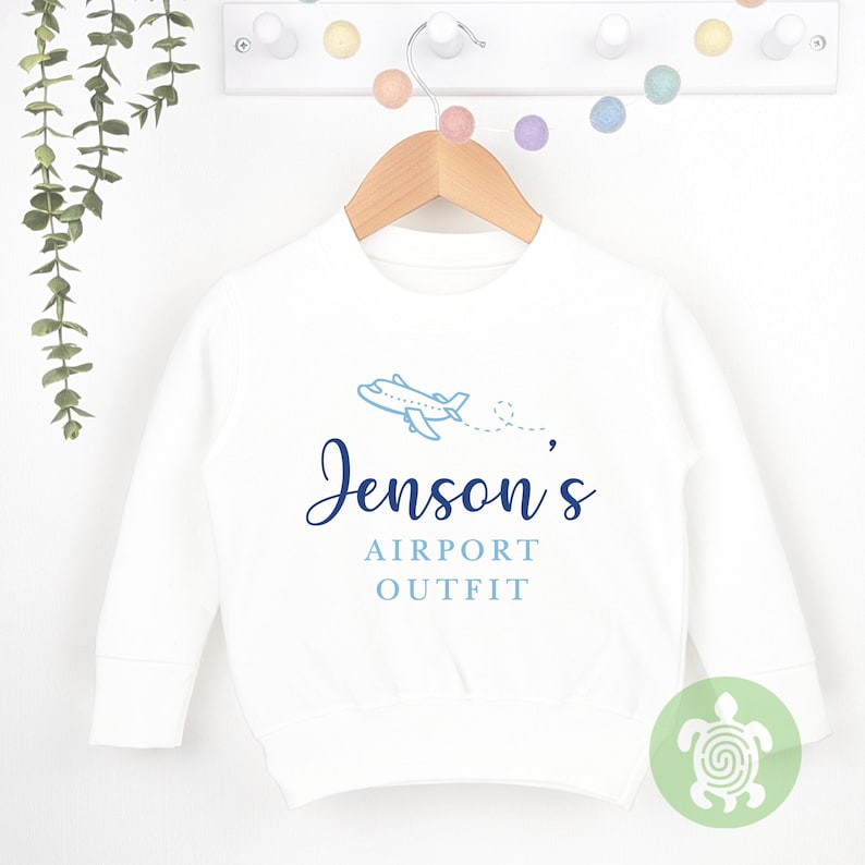 May include: White long-sleeve sweatshirt with a blue airplane graphic and the text "Jenson's Airport Outfit".