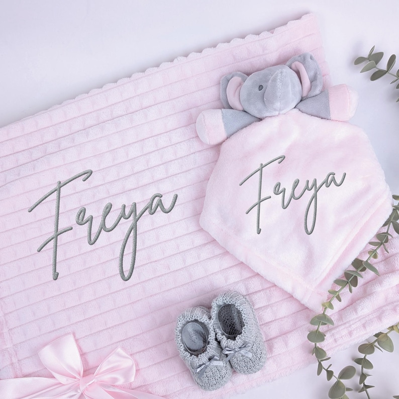 Puede incluir: Un juego de regalo para beb&eacute; con una manta rosa y un arrullo de elefante a juego, ambos con el nombre "Freya" bordado. El juego incluye patucos grises para beb&eacute; y una cinta rosa.