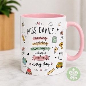 May include: A white ceramic mug with a light pink interior and handle. The exterior features the text MISS DAVIES followed by teaching, inspiring, encouraging, making a DIFFERENCE, every day, surrounded by colorful school-themed icons.