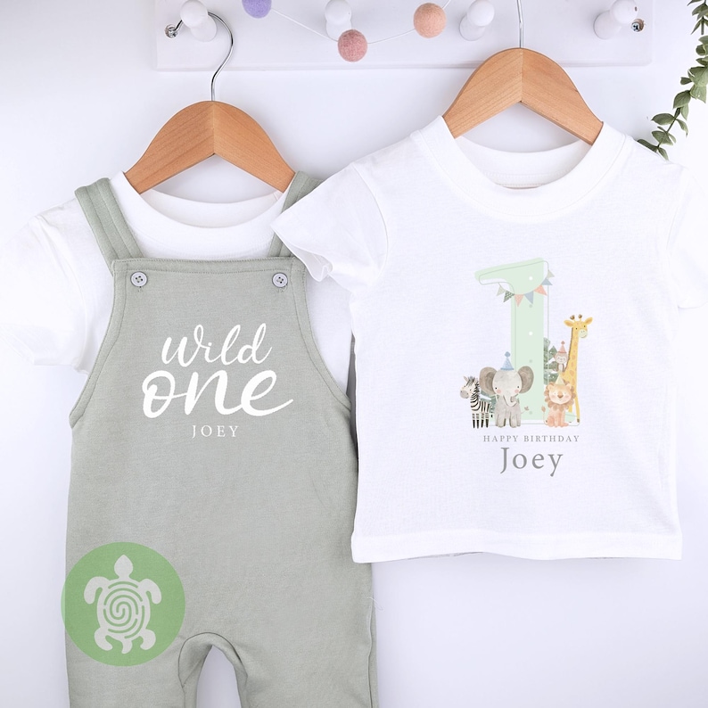 May include: A white t-shirt with a green number one and animal illustrations. The text "Happy Birthday Joey" is printed below the number. A green and white jumpsuit with the text "Wild One Joey" is also shown.