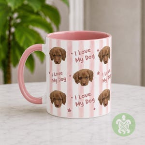 May include: A ceramic mug with a pink handle and interior, featuring a repeating pattern of light pink vertical stripes, small stars, and the text I Love My Dog alongside a photographic portrait of a brown puppy on the white exterior surface.