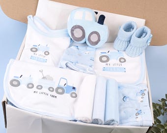 Puede incluir: Una caja de regalo con artículos para bebé con temática de tractor azul. Incluye un body blanco, un babero, un juguete de peluche de tractor, patucos de punto azul claro, un gorro estampado, tres paños doblados y una manta, con el texto My Little Farm.