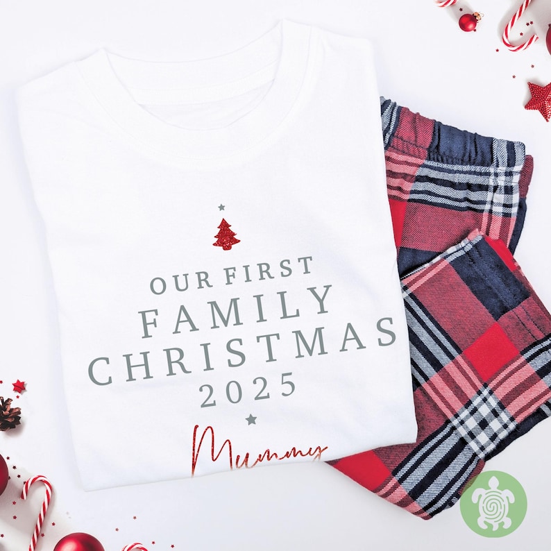 May include: A white t-shirt featuring the grey text "OUR FIRST FAMILY CHRISTMAS 2025" with a small red glittery Christmas tree icon above and the word "Mummy" in red script below, paired with red, black, and white plaid pajama pants.