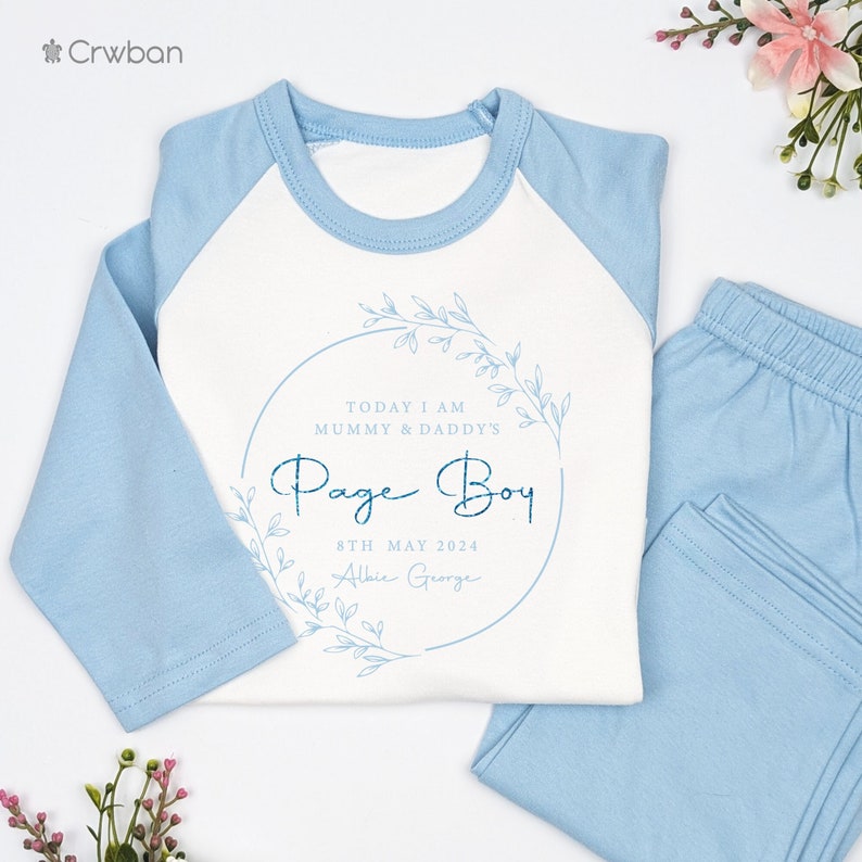May include: A light blue and white pajama set. The top has light blue sleeves and a white body with the text "Today I am Mummy & Daddy's Page Boy" inside a floral wreath. The matching pants are light blue.