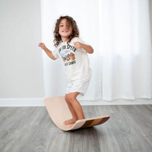 Child balancing on a wooden wobble board indoors, enhancing motor skill development and coordination.