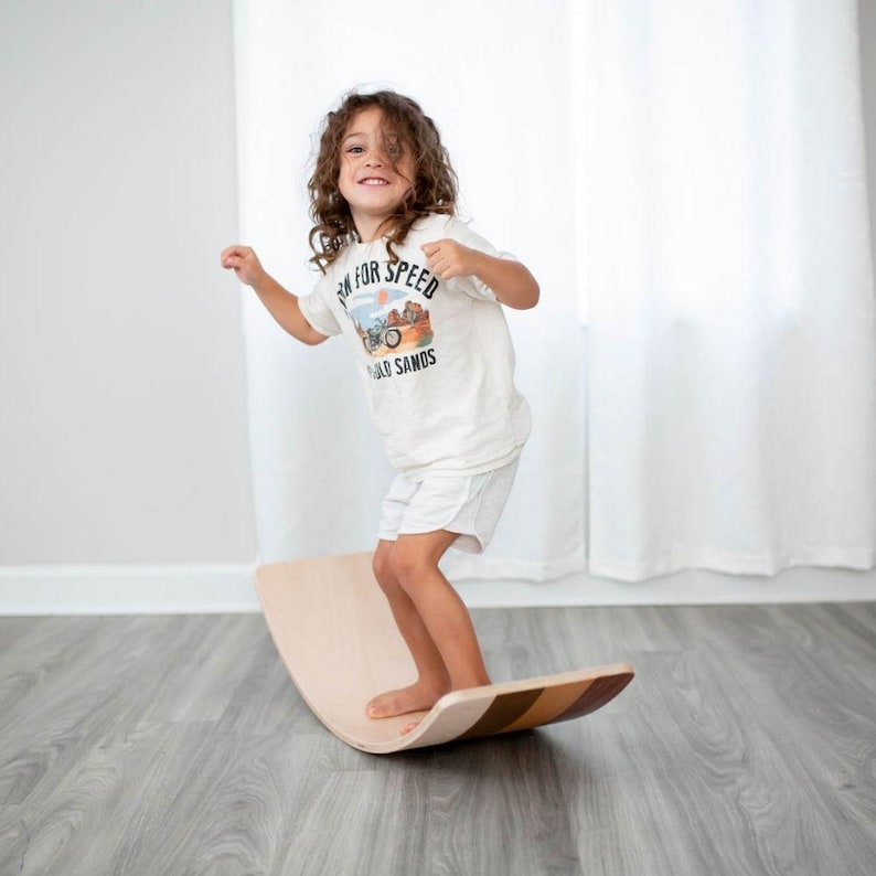 Child balancing on a wooden wobble board indoors, enhancing motor skill development and coordination.