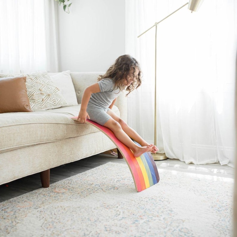 Child sliding down a wooden wobble board, engaging in active play, developing balance and coordination, and enjoying imaginative pretend play.
