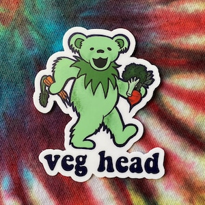 May include: Green cartoon bear holding a carrot and broccoli with the text "veg head" in a blue and white font.