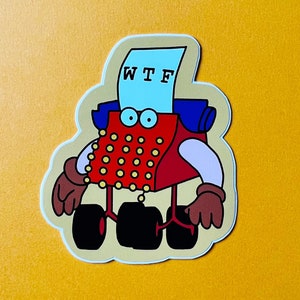 May include: A red and blue typewriter with a paper that says "WTF" on it. The typewriter has wheels and is wearing brown gloves. The sticker is on a yellow background.