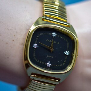 Caravelle ,gold tonewith black dial, quartz wrist watch on stretch bracelet
