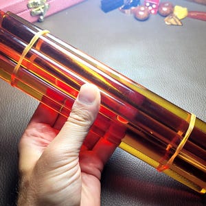 May include: A bundle of five translucent amber-coloured cylindrical rods held together by two thin rubber bands. The rods are smooth, straight, and uniform in length, exhibiting a deep orange-brown hue that allows light to pass through the material.