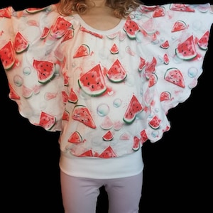 Könnte beinhalten: Weißes Oberteil mit Wassermelonen-Scheibenmuster. Das Oberteil hat einen Rundhalsausschnitt und ein lockeres, fließendes Design. Die Wassermelonen-Scheiben sind rot mit grünen Schalen.