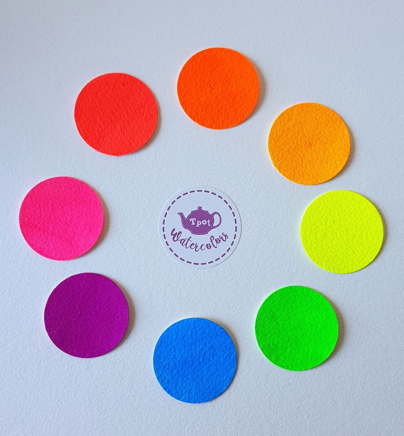 May include: A collection of eight colorful felt circles arranged in a circular pattern. The colors include red, orange, yellow, green, blue, purple, and pink. A circular sticker in the center reads "Tpot Watercolors".
