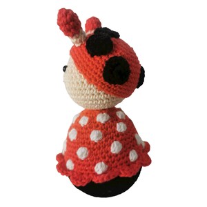 以下が含まれることがあります： 赤と白のドット柄のドレスと黒い斑点のある、かぎ針編みで作られたテントウムシのドール。ドールは白い顔と黒い目を持っている。