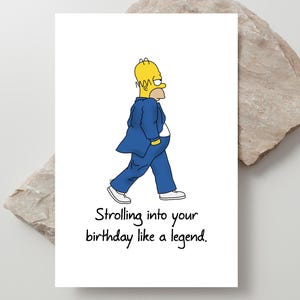 Puede incluir: Tarjeta de felicitación blanca con un personaje de dibujos animados con traje azul y pelo amarillo. El texto de la tarjeta dice: "Strolling into your birthday like a legend."