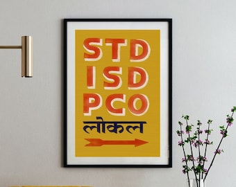 May include: A yellow armchair with black legs sits in front of a framed print with the text "STD ISD PCO लोकल" in red and orange letters on a yellow background. The print is hanging on a white wall.