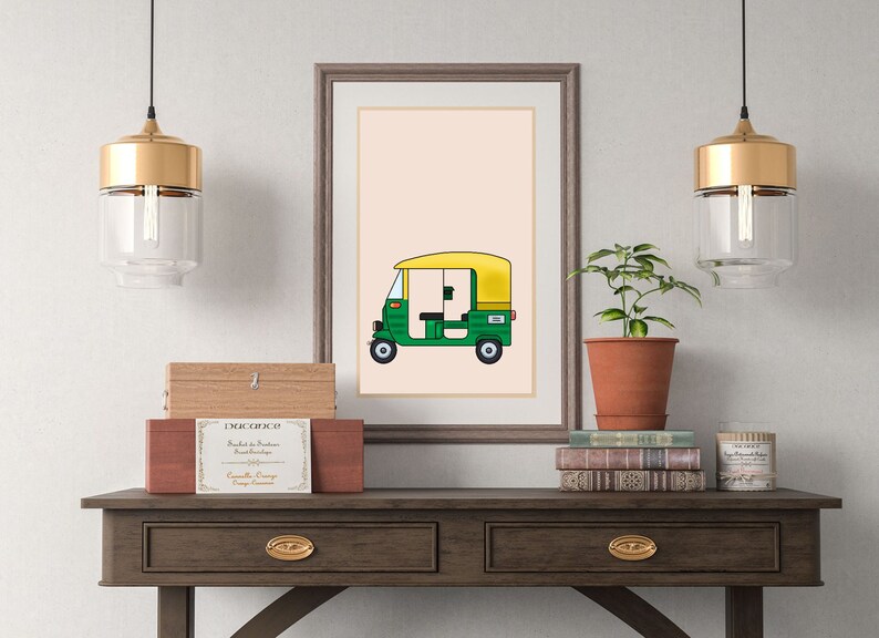 May include: A framed illustration of a green and yellow auto rickshaw, also known as a tuk-tuk, on a light pink background. The illustration is hanging on a wall above a wooden table with two drawers.