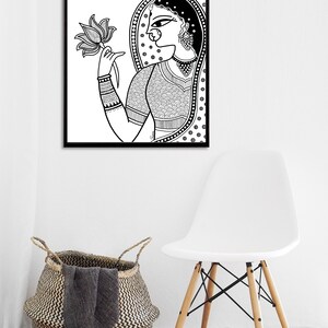 May include: Black and white line art print of a woman in traditional Indian clothing holding a lotus flower. The woman is wearing a patterned sari and jewelry. The print is framed in a black frame.