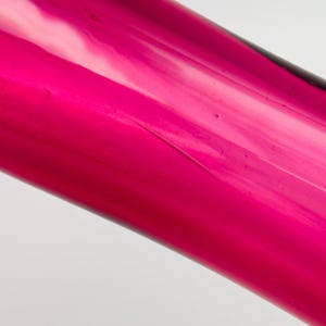 Puede incluir: Primer plano de un jarr&oacute;n de vidrio rosa oscuro con una superficie lisa y brillante.