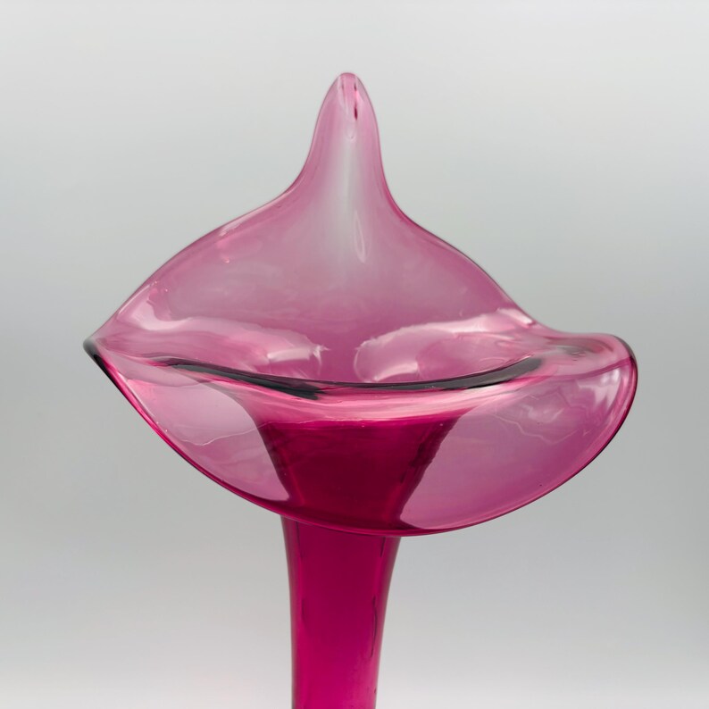 Puede incluir: Un jarr&oacute;n de vidrio rosa con forma de lirio calla. El jarr&oacute;n tiene una abertura ancha y acampanada y un cuello largo y delgado.