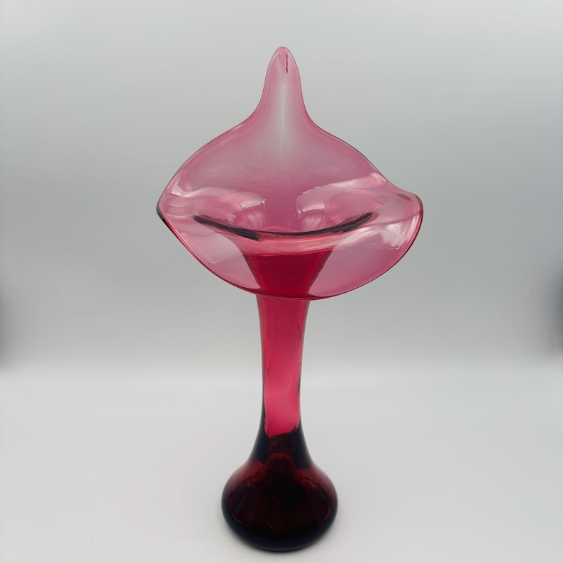 Puede incluir: Un jarr&oacute;n de vidrio rosa con una abertura ancha y acampanada y un cuello largo y delgado. El jarr&oacute;n tiene un color profundo y rico y un acabado liso y pulido.