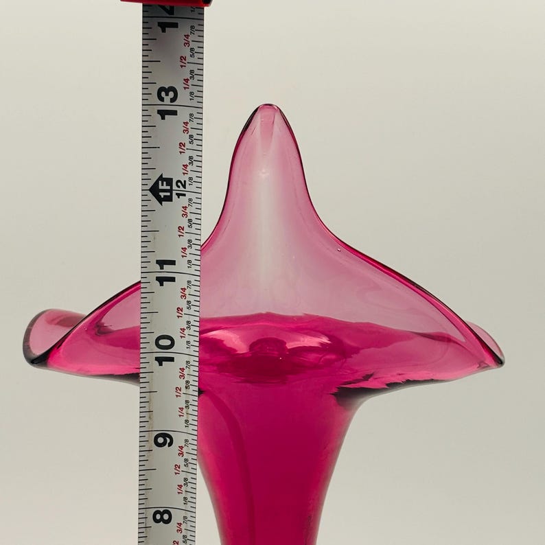 Puede incluir: Un jarr&oacute;n de vidrio rosa oscuro con una abertura ancha y acampanada y una base estrecha. El jarr&oacute;n mide aproximadamente 28 cm de alto.