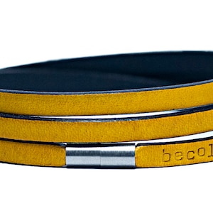 Puede incluir: Un brazalete de cuero amarillo mostaza con un cierre de plata y el texto "becolours" grabado en el cuero.