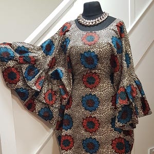 May include: A patterned dress with flared sleeves and a round neckline. The dress features a repeating floral design in red and blue on a cream and brown background. A silver chain necklace is around the mannequin's neck.