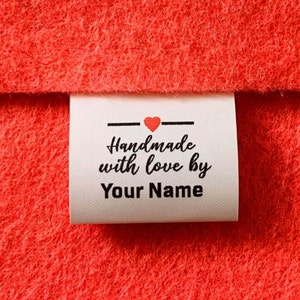 May include: White fabric label with black text that reads "Handmade with love by Your Name". A small red heart is above the text.
